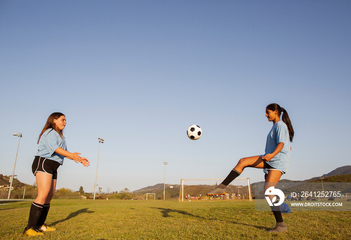 Side view of players practicing soccer on grassy field against clear blue sky