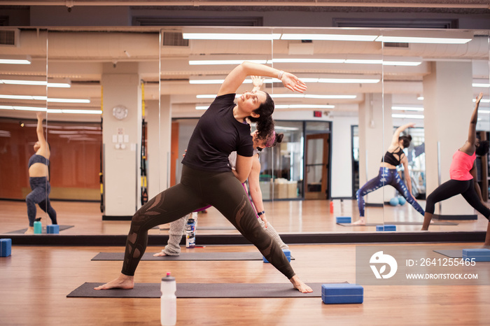 Female athletes practicing extended side angle pose on exercise mats against mirror in gym