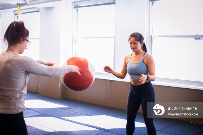 Female athletes exercising with medicine ball against windows in gym