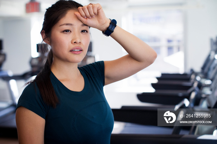 Thoughtful female athlete standing on treadmills in gym