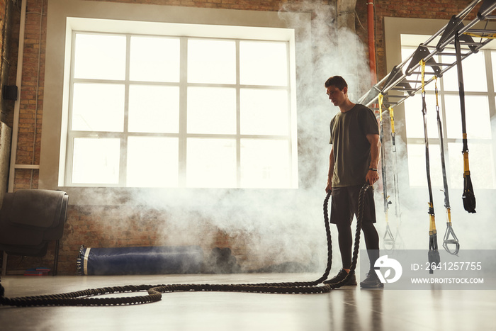 Never stop. Side view of young athletic man with perfect body doing crossfit exercises with a rope i