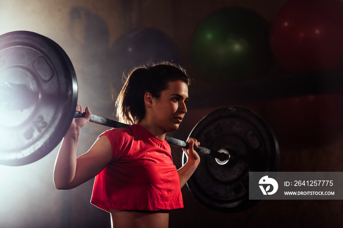 Young athletic woman pumping up muscles in crossfit gym