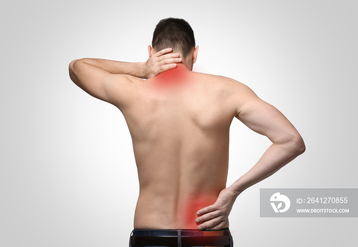 Young man suffering from back pain on light background. Health care concept
