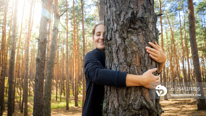 Portrait of beautiful smiling young woman leaning and hugging big old tree in forest. Concept of lov