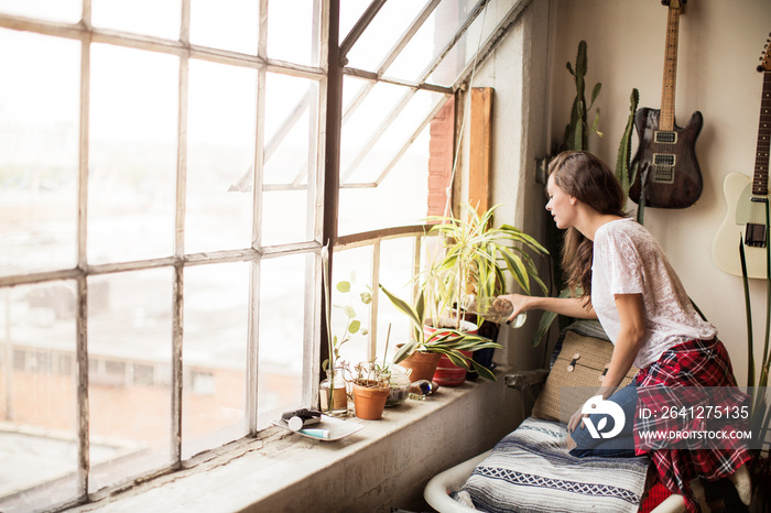 Side view of young woman watering plants at home