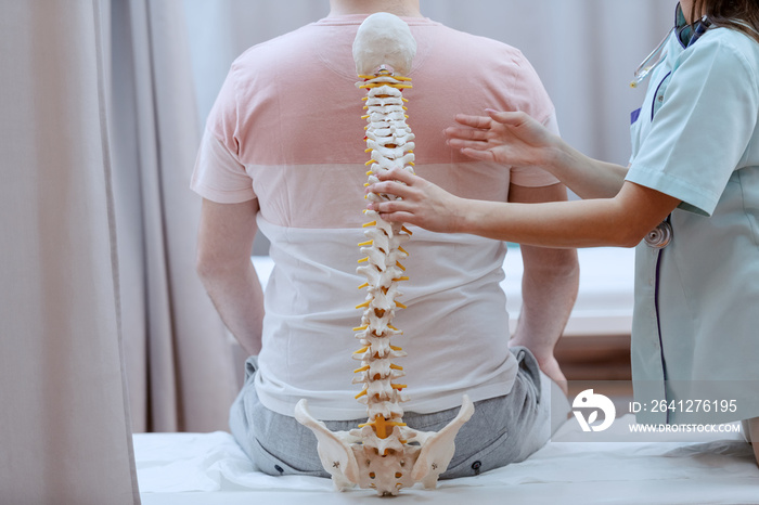 Caucasian nurse holding spine model against the patients backs. Clinic interior.