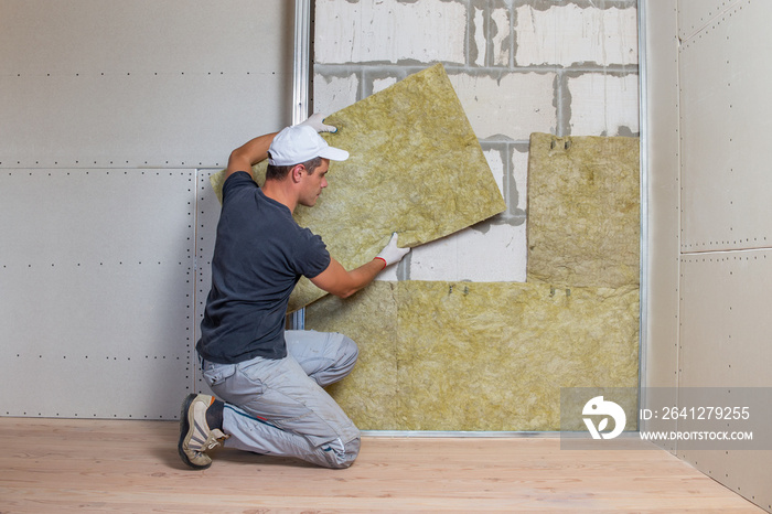 Worker insulating a room wall with mineral rock wool thermal insulation.