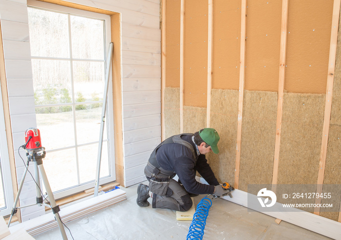 The worker makes finishing works of walls with a white wooden board, using laser line level. Buildin