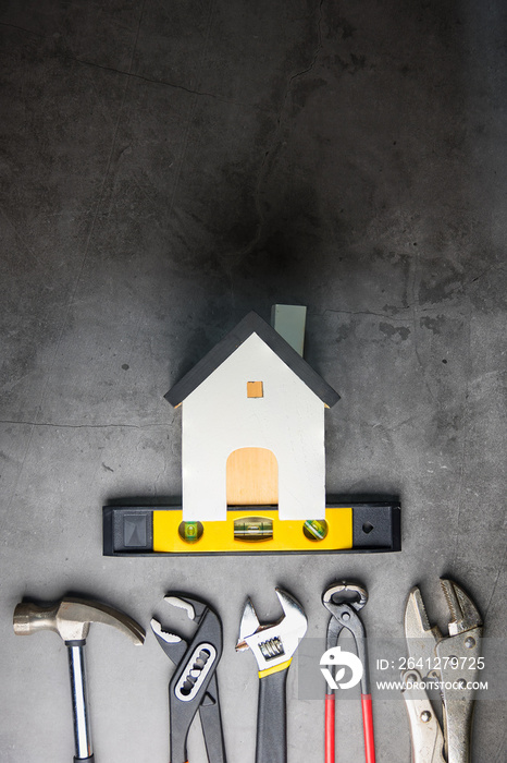 灰黑色水泥地板背景上的木制白色房屋玩具和建筑工具，带有复制空间。