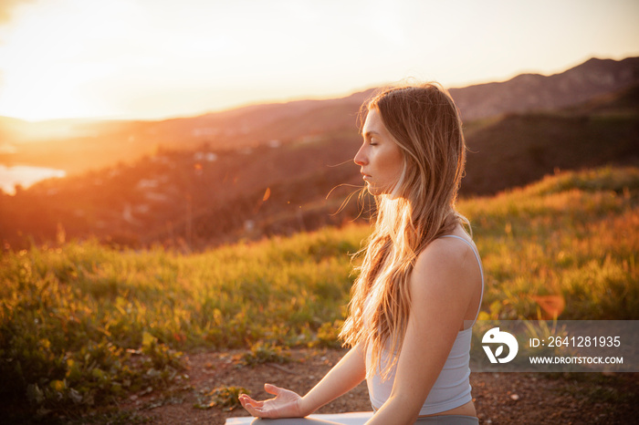 Female athlete with eyes closed meditating on mountain during sunset