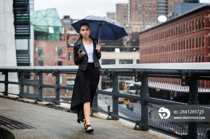 Front view of woman carrying umbrella while walking on bridge in city