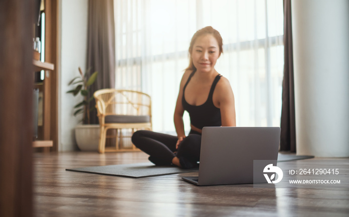 一位美丽的年轻亚洲女性在家里用笔记本电脑观看在线锻炼教程