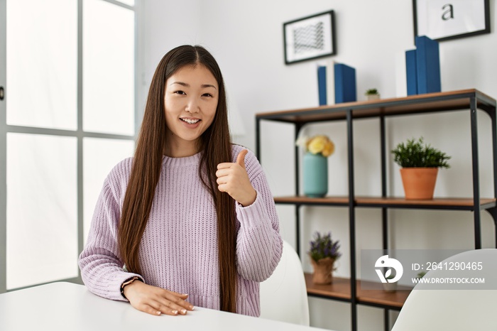 年轻的中国女孩穿着休闲服坐在家里的桌子上，微笑着快乐而积极，t