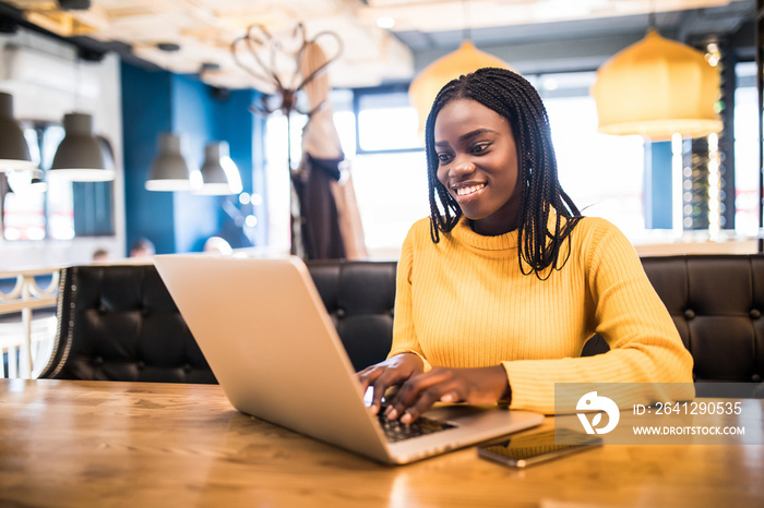 African american woman with laptop and phone in a cafe