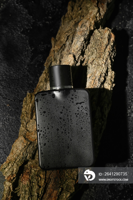 Perfume bottle covered with water drops on dark background