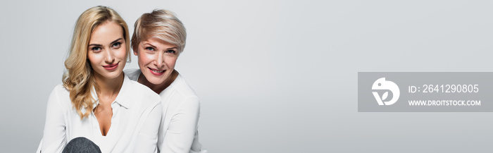 mature woman with adult daughter smiling at camera isolated on grey, banner