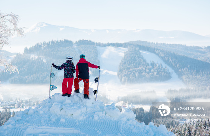 Two snowboarders enjoy the snow-white scenery of mountains and forests of the Carpathians from the h