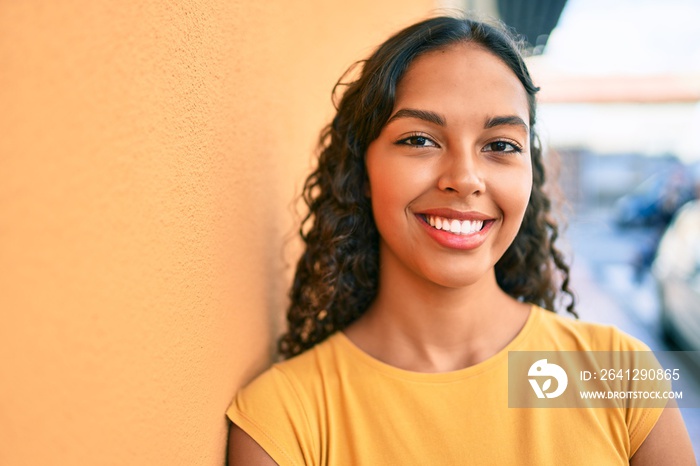 Young african american girl smiling happy leaning on the wall at city.