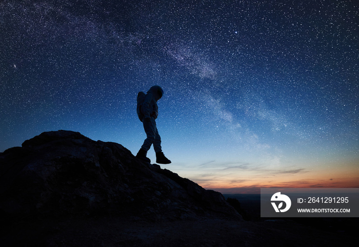 Full length of astronaut walking down the mountain under beautiful night sky with stars. Silhouette 