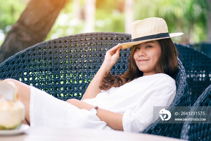 一位戴着帽子的亚洲美女的肖像画，她躺在花园里的长椅上，手里拿着椰子