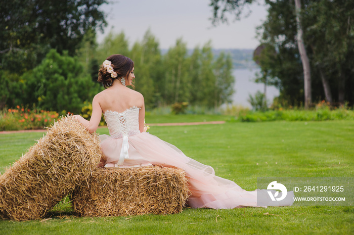 一位美丽的新娘在户外拿着花束的肖像。一位可爱的女士背靠压着的稻草坐着