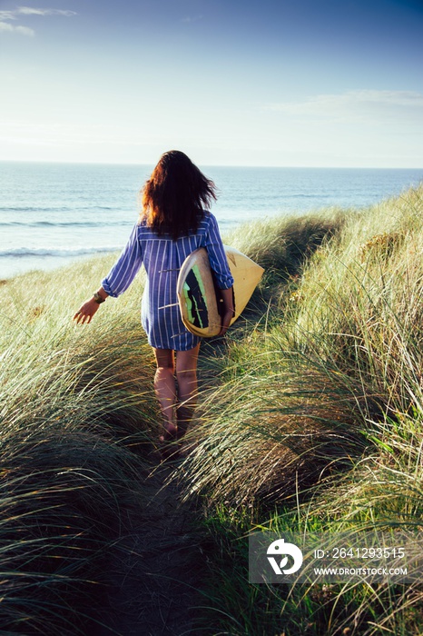 Vertical shot of a brunette woman walking to the beach to surf in the wavy ocean