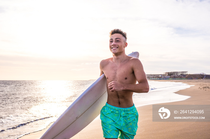 英俊的年轻人带着冲浪板在海滩上行走，准备乘风破浪的肖像