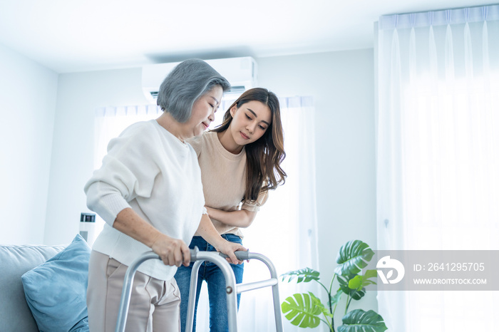 Asian daughter support older woman grandma walk with walker at home. 