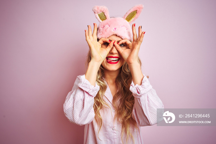 Young beautiful woman wearing pajama and sleep mask over pink isolated background doing ok gesture l