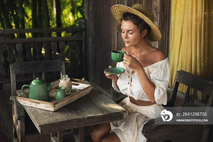 Happy woman sitting on the summer terrace and drinking coffee