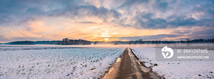 Landscape panorama with road, white fields cover by snow and sunset sky.