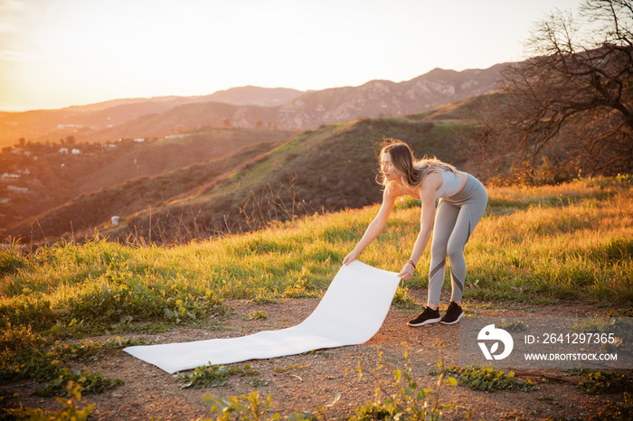 Full length of sportswoman holding exercise mat on mountain during sunset