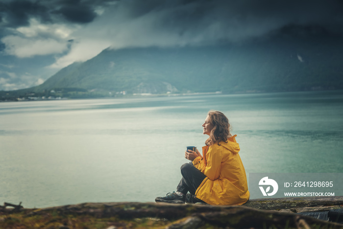 一个年轻漂亮的女孩在峡湾岸边喝茶，去北欧美女挪威旅行