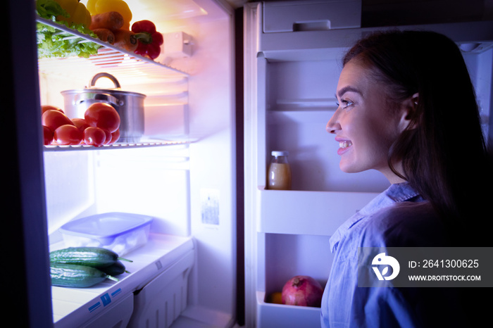 Millennial woman raiding refrigerator late at night