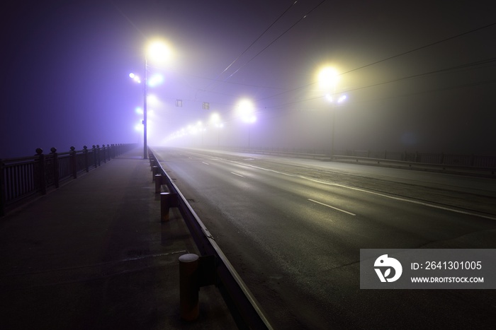 夜间浓雾中穿过照亮的空石桥的人行道和高速公路。L