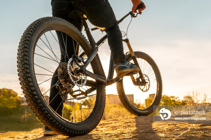 Man on mountain bike. Bicycle wheels close up image on sunset. Low angle view of cyclist riding moun