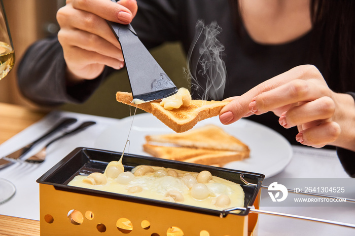 the girl tastes cheese raclette in a cafe. Delicious and with hot steam. swiss food. cheese raclette