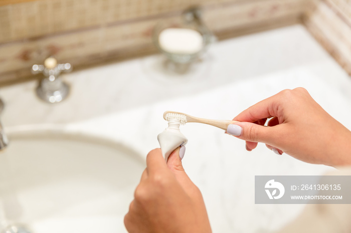 Cropped image of attractive woman hand applying toothpaste on toothbrush in bathroom. Beauty healty 