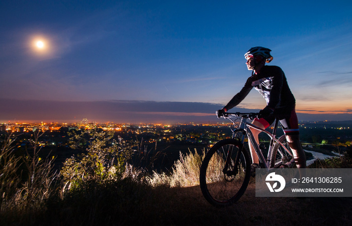 骑山地自行车的年轻运动员，在山顶上观察傍晚的城市景观。