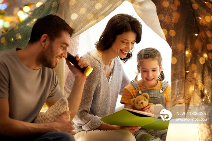 family, hygge and people concept - happy mother, father and little daughter reading book with torch 