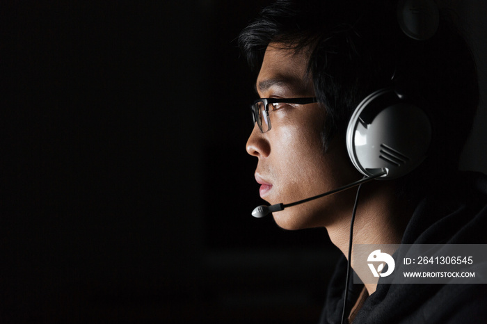 Serious young man using headset in dark room