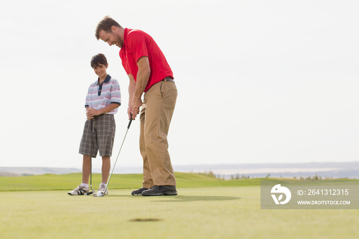 Preteen boy watching father make golf putt