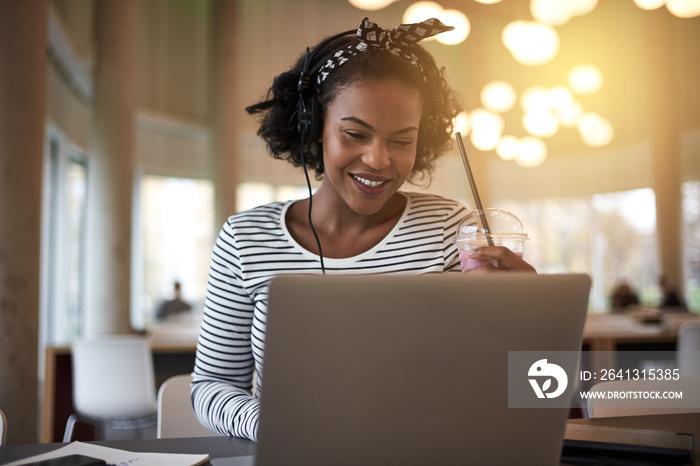 Smiling African college student drinking a smoothie while studyi