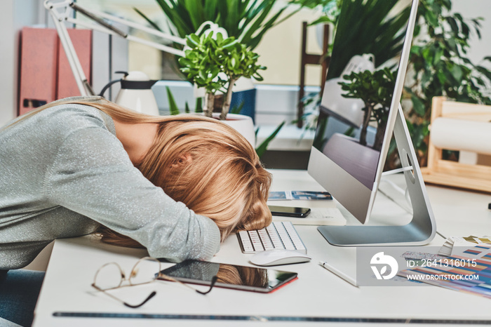 年轻的金发女人在办公室加班后睡在键盘上。