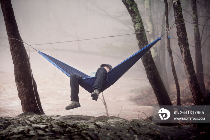 Young male hiker relaxing in hammock next to river