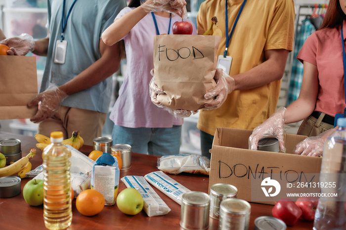 Cropped shot of male and female volunteers holding paper bag with food while packing donation for ne