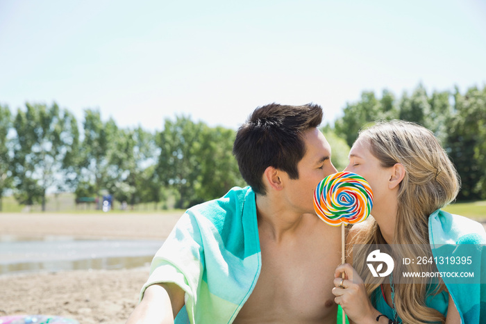 Young couple kissing behind lollypop on the beach