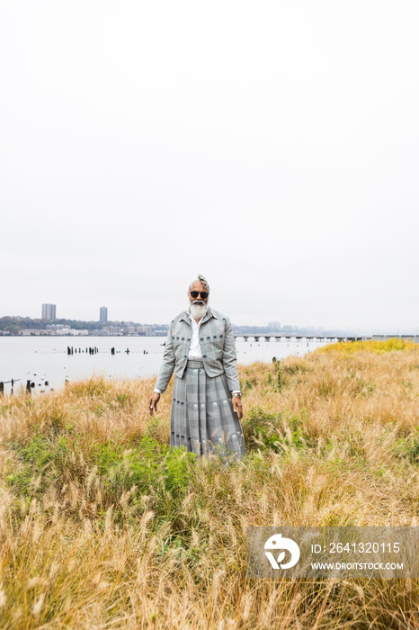 man with gray hair and beard wearing skirt suit in waterfront natural area