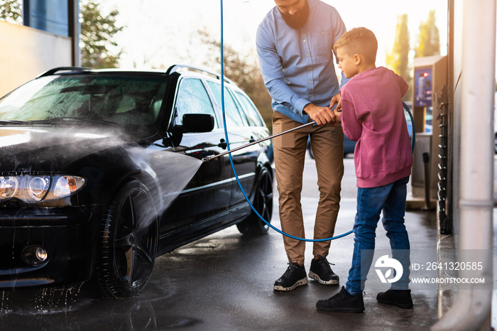 Father and son washing their car at car wash station using high pressure water.