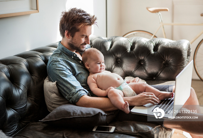 Smiling father with his daughter using laptop on sofa